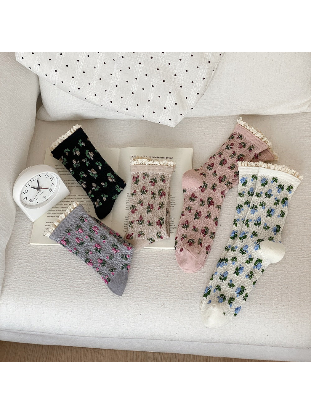 Black, gray, beige, pink and ivory floral socks with cream ruffled cuffs arranged on a sofa.