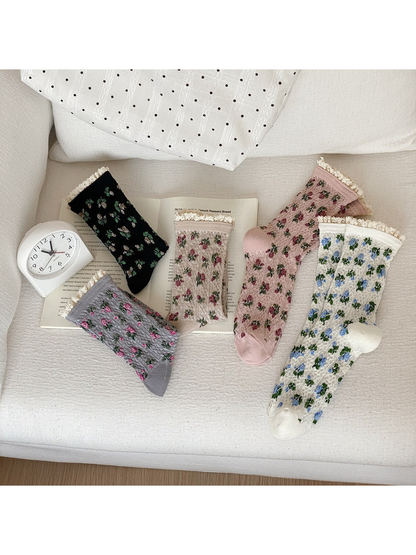 Black, gray, beige, pink and ivory floral socks with cream ruffled cuffs arranged on a sofa.