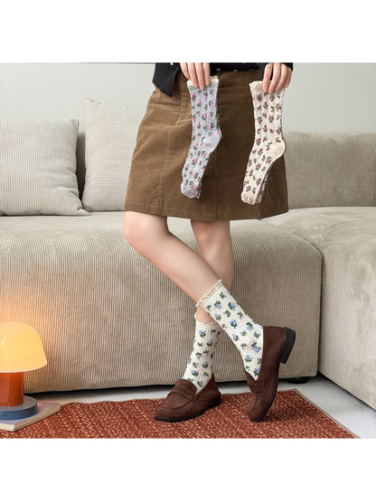 Ivory floral socks worn with brown loafers while gray and beige floral socks are held above.