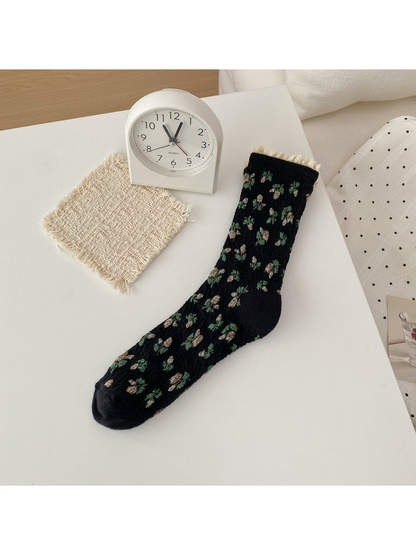 Black sock with cream flowers, green leaves and a cream ruffled cuff.