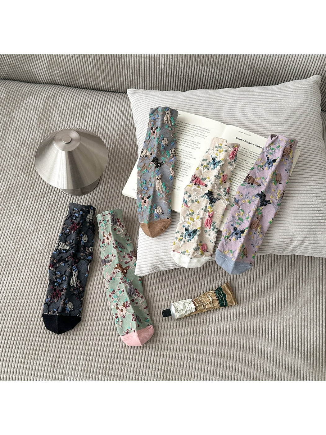 Five colors of socks with animal and botanical patterns arranged on a sofa.