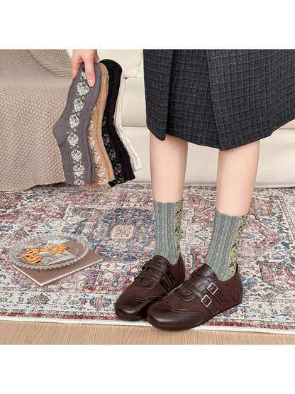 Green patterned socks worn with brown buckle shoes, with other sock colors held beside them.