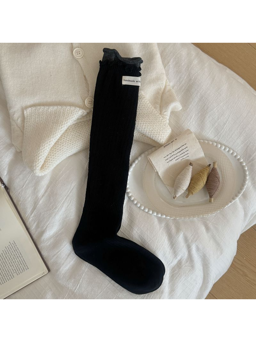 Black sock with diamond pointelle, vertical ribbing, a ruffled edge and contrasting dark gray cuff.