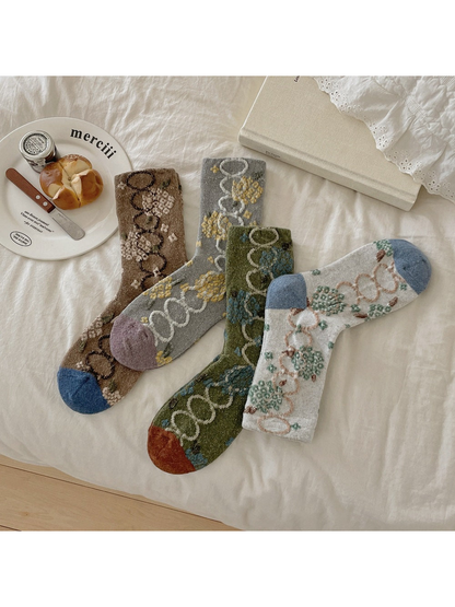 Four color variations of floral and linked-oval socks arranged on white bedding.