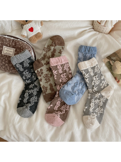 Floral socks in Green, Pink, Black Gray, Blue and Gray arranged on white bedding.