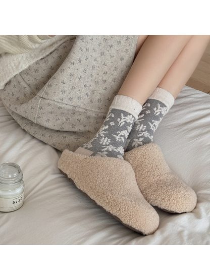 Gray floral socks with ivory cuffs worn with beige slippers on white bedding.