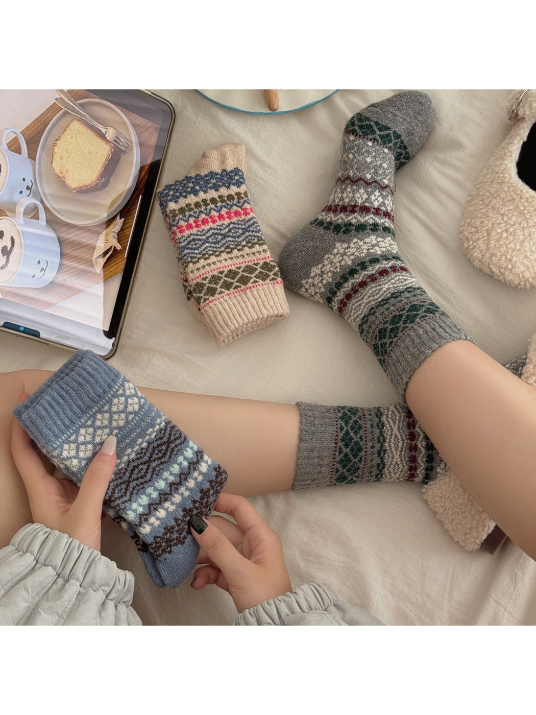Gray geometric patterned socks worn while a folded Blue sock is held beside a folded Beige sock.