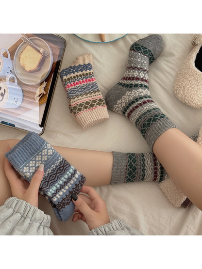 Gray geometric patterned socks worn while a folded Blue sock is held beside a folded Beige sock.