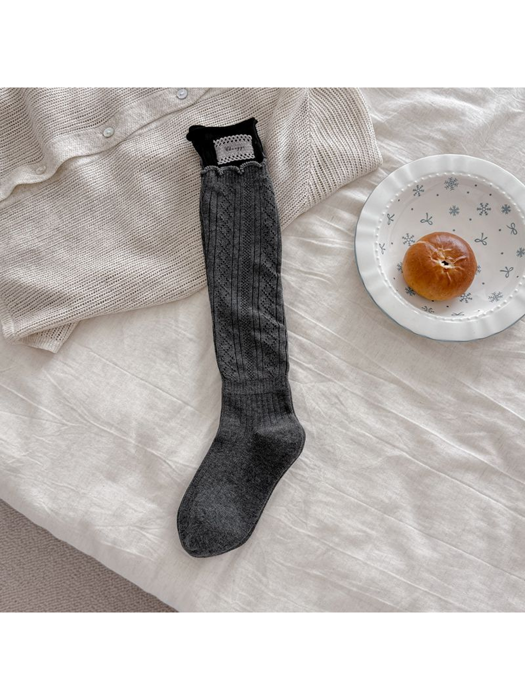 Gray pointelle sock laid flat with a black upper cuff, pale rectangular patch, and scalloped edging.