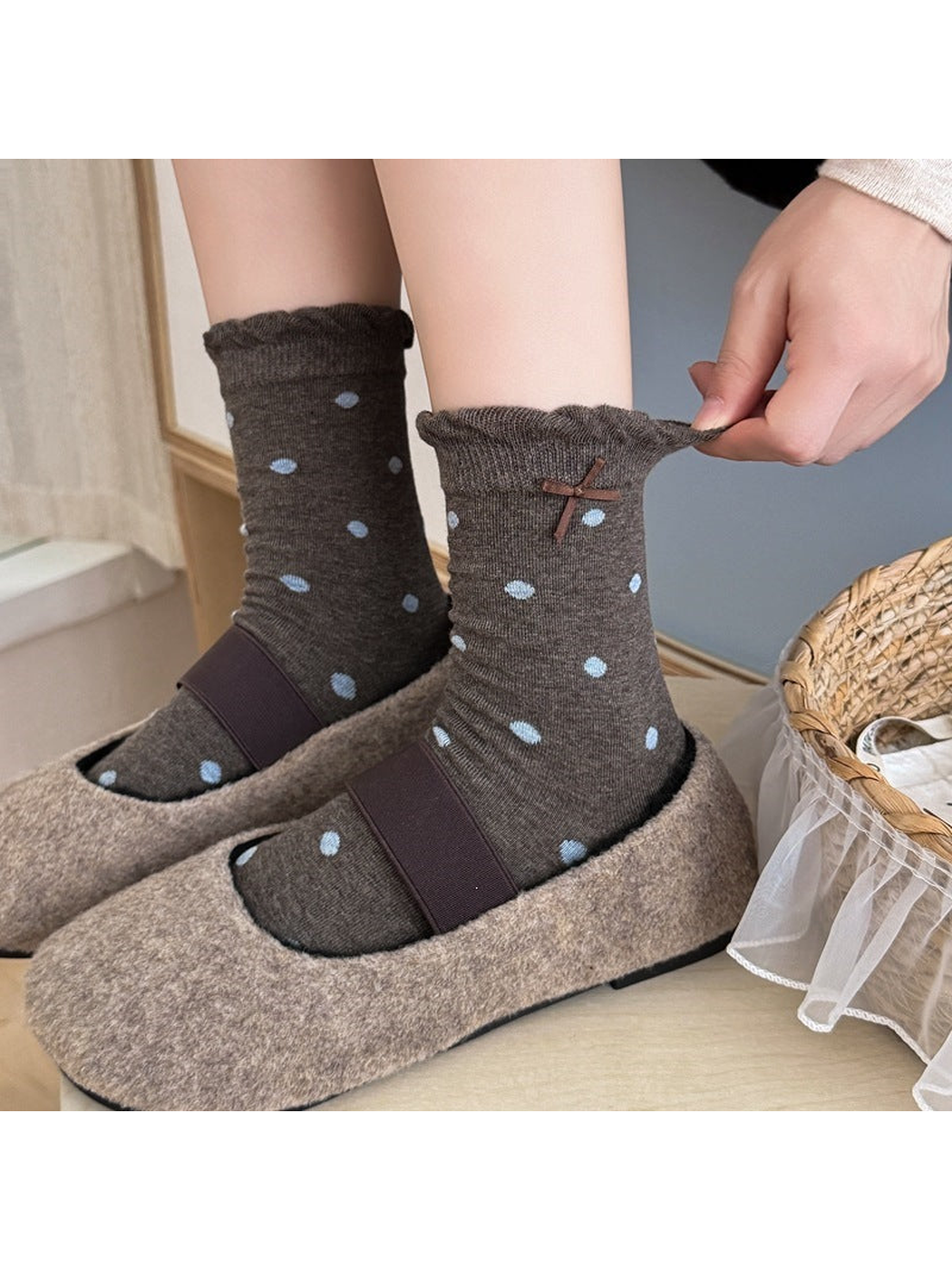 Gray socks with large blue dots worn with shoes as a hand stretches one ruffled cuff.
