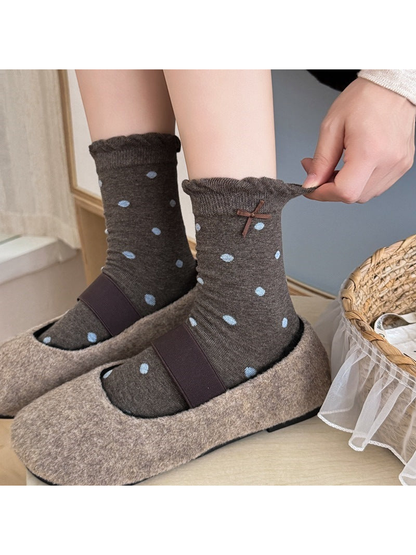 Gray socks with large blue dots worn with shoes as a hand stretches one ruffled cuff.