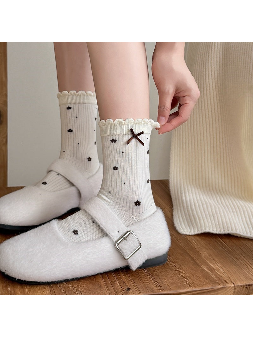 Ivory floral socks worn with white shoes as a hand holds one scalloped cuff.
