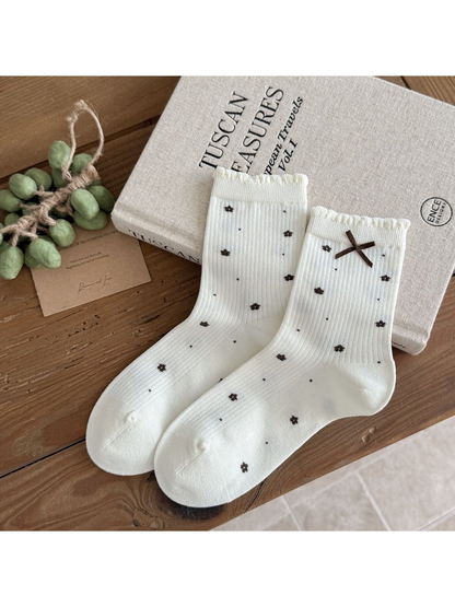 Ivory Flowers socks with dark floral motifs, vertical ribbing, scalloped cuffs and a brown ribbon bow.