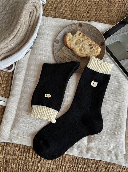 Black socks with ivory ribbed cuffs and cat face and fish emblems, shown flat and folded.