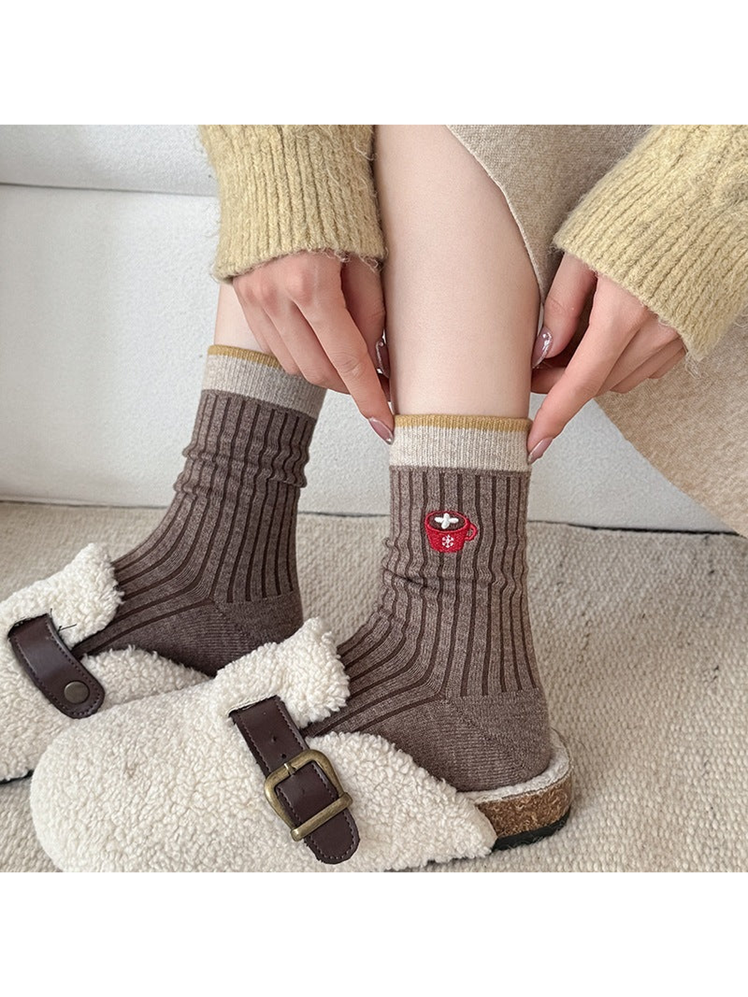Brown Coffee Cup socks worn with slippers, with hands pulling the contrasting cuff.