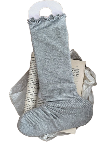 Light Gray sock with a ruffled cuff and ribbed ankle and foot displayed in a woven basket.