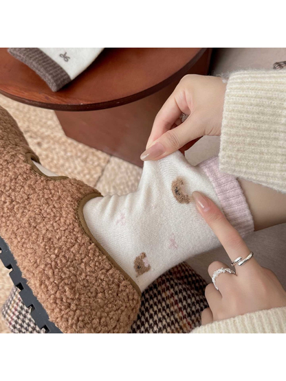 Hands pull the fabric of a pink-trim sock worn with a brown shoe, showing a fuzzy bear-head motif.