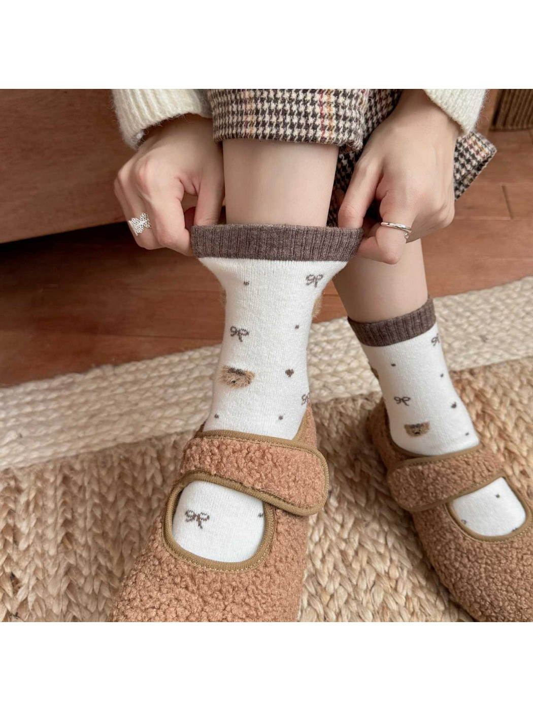 Brown-trim bear-pattern socks worn with brown shoes while hands stretch one ribbed cuff.