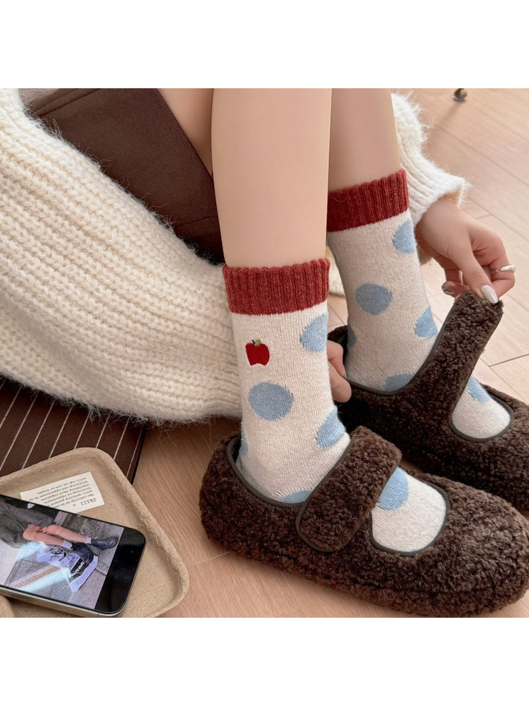 Person wearing Apple socks with blue polka dots while adjusting brown slippers.