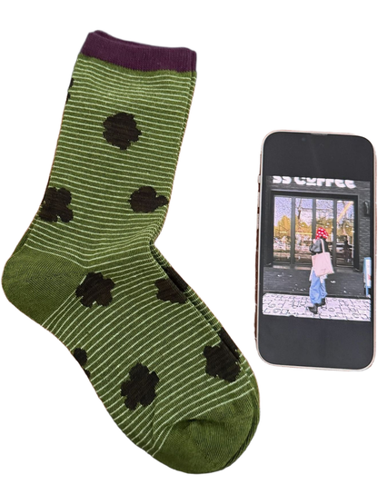 Green sock with fine pale stripes, dark flowers and a purple cuff.