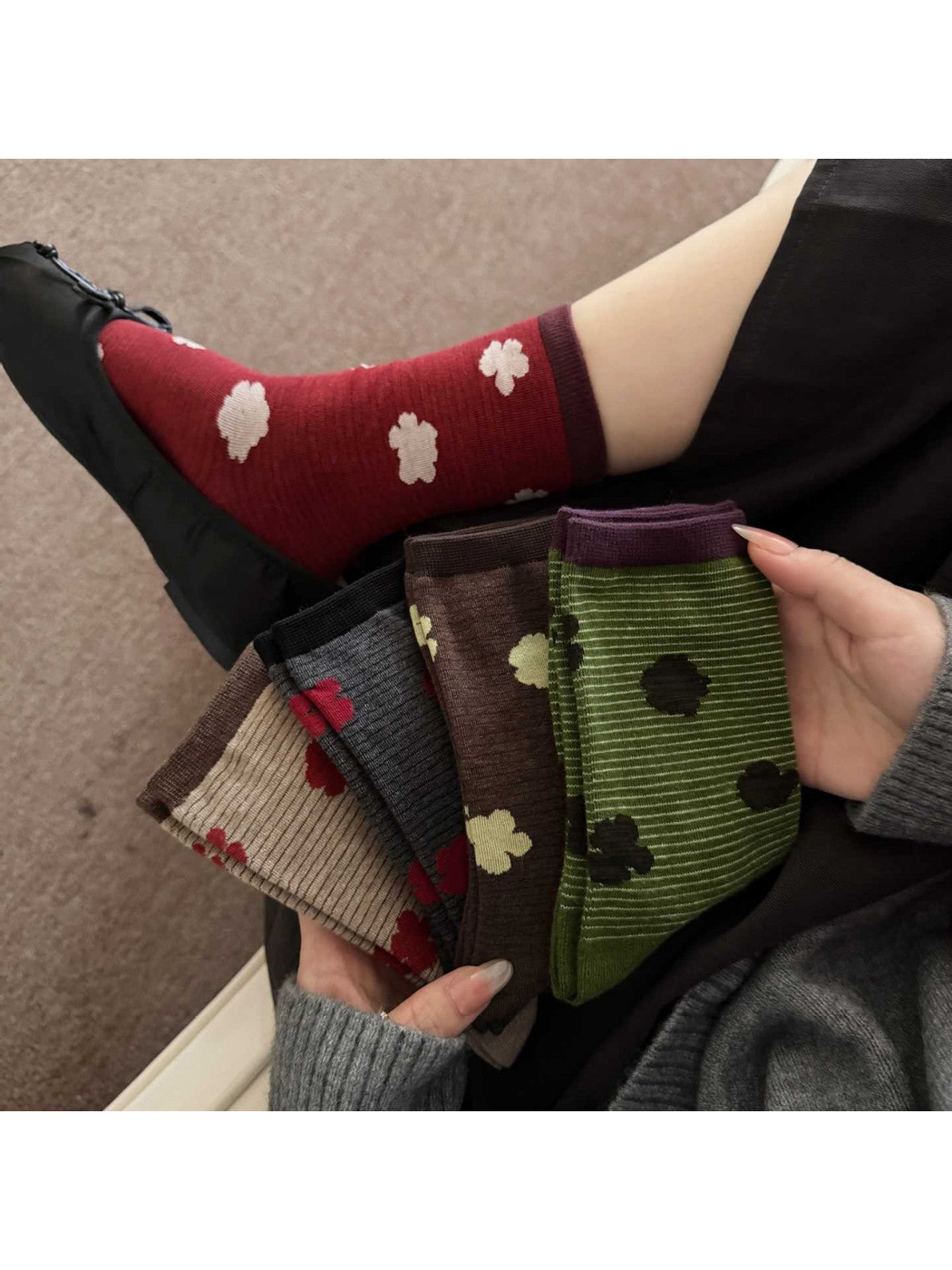 Burgundy floral sock worn with a black shoe while hands hold several other floral socks.