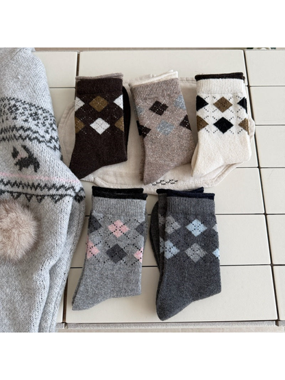 Folded argyle socks in Light Gray, Dark Gray, Ivory, Black and Brown arranged on a tiled surface.