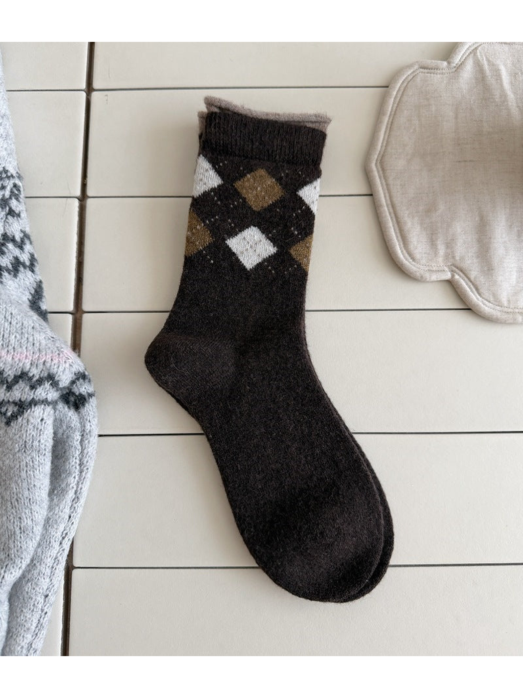Black sock with brown and light argyle diamonds, a ribbed cuff and a taupe top edge.