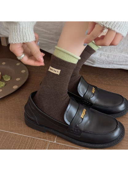 Brown socks with pale green rolled cuffs worn with black loafers as a hand stretches one cuff.
