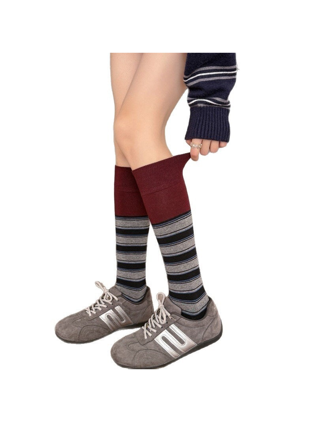 Red striped socks worn with gray shoes while a hand pulls one cuff outward.