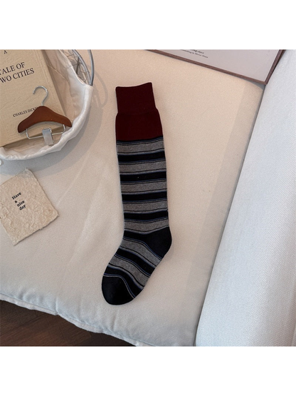 Red sock laid flat with a wide ribbed cuff, gray and black stripes, and black toe and heel.