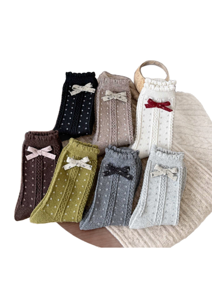 Seven colors of dotted socks with vertical cable-textured bands, scalloped cuffs, and contrasting bows.