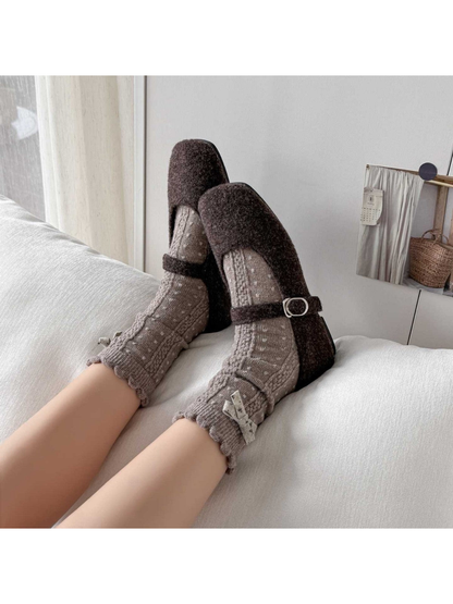 Greige dotted socks with scalloped cuffs and bows worn with dark strap shoes on a sofa.