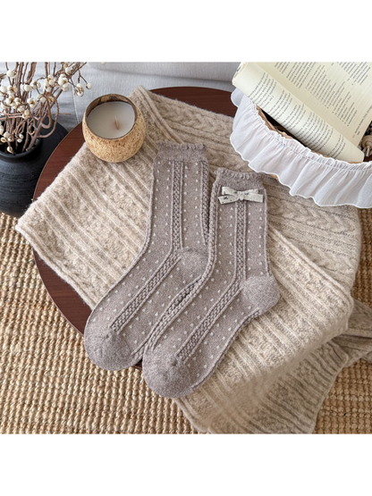 Greige socks with small light dots, cable-textured bands, scalloped cuffs, and a cream bow.