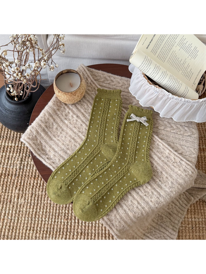 Green socks with small light dots, cable-textured bands, scalloped cuffs, and a cream bow.