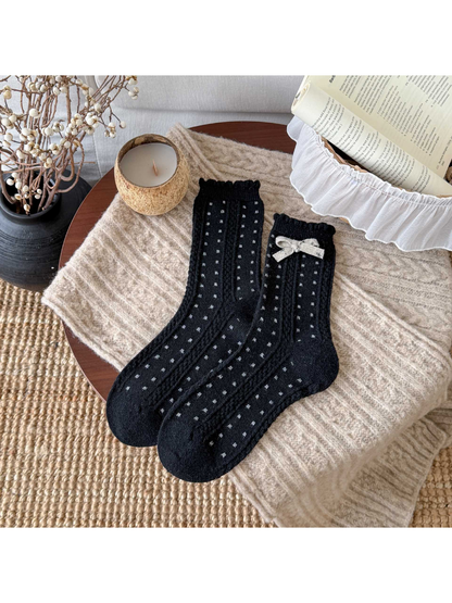 Black socks with small light dots, cable-textured bands, scalloped cuffs, and a cream bow.