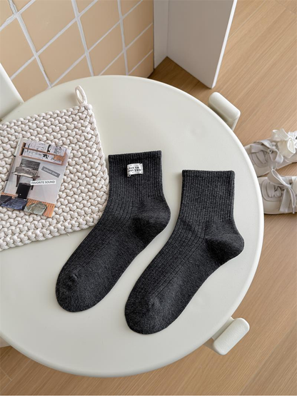 Dark gray Label socks with ribbed cuffs and a small white text label arranged on a chair.