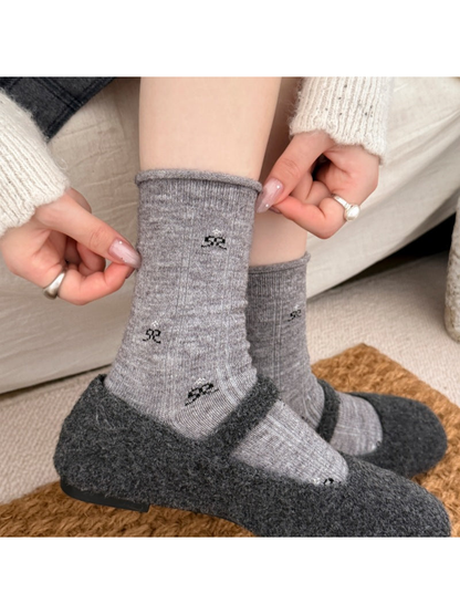 Gray bow-patterned socks worn with dark shoes while hands pull the cuff.