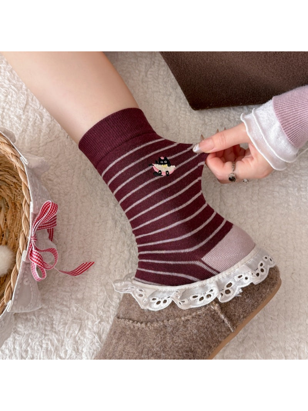 Burgundy striped sock with a cat motif being pulled outward above a lace-trimmed slipper.