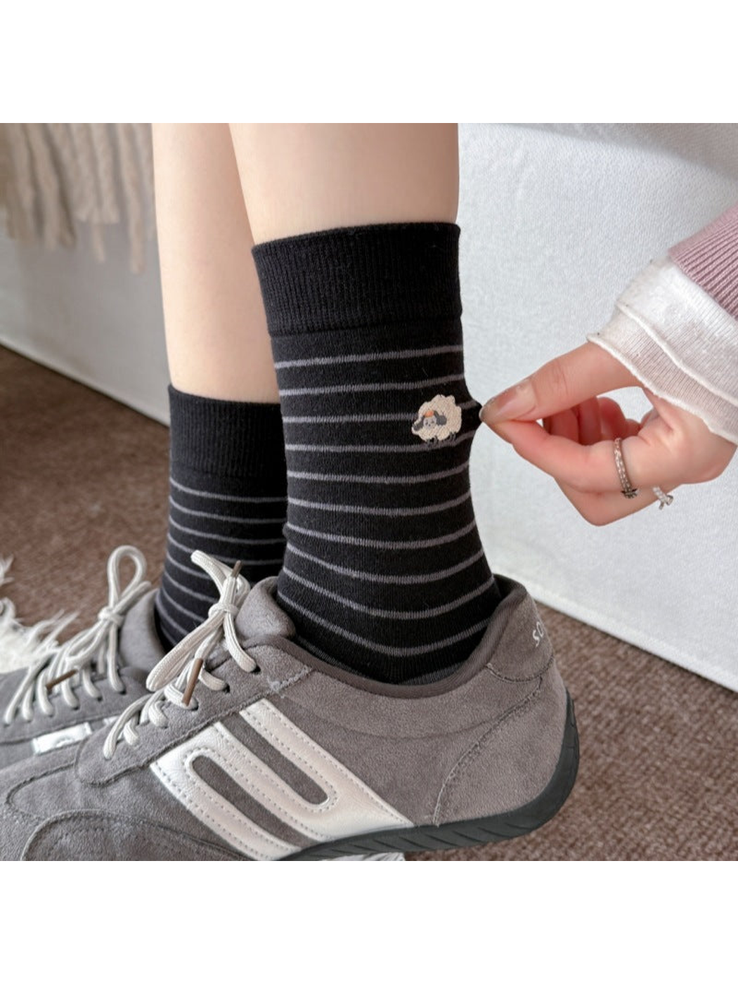 Black striped socks worn with gray sneakers, with a hand pulling the fabric beside the sheep motif.