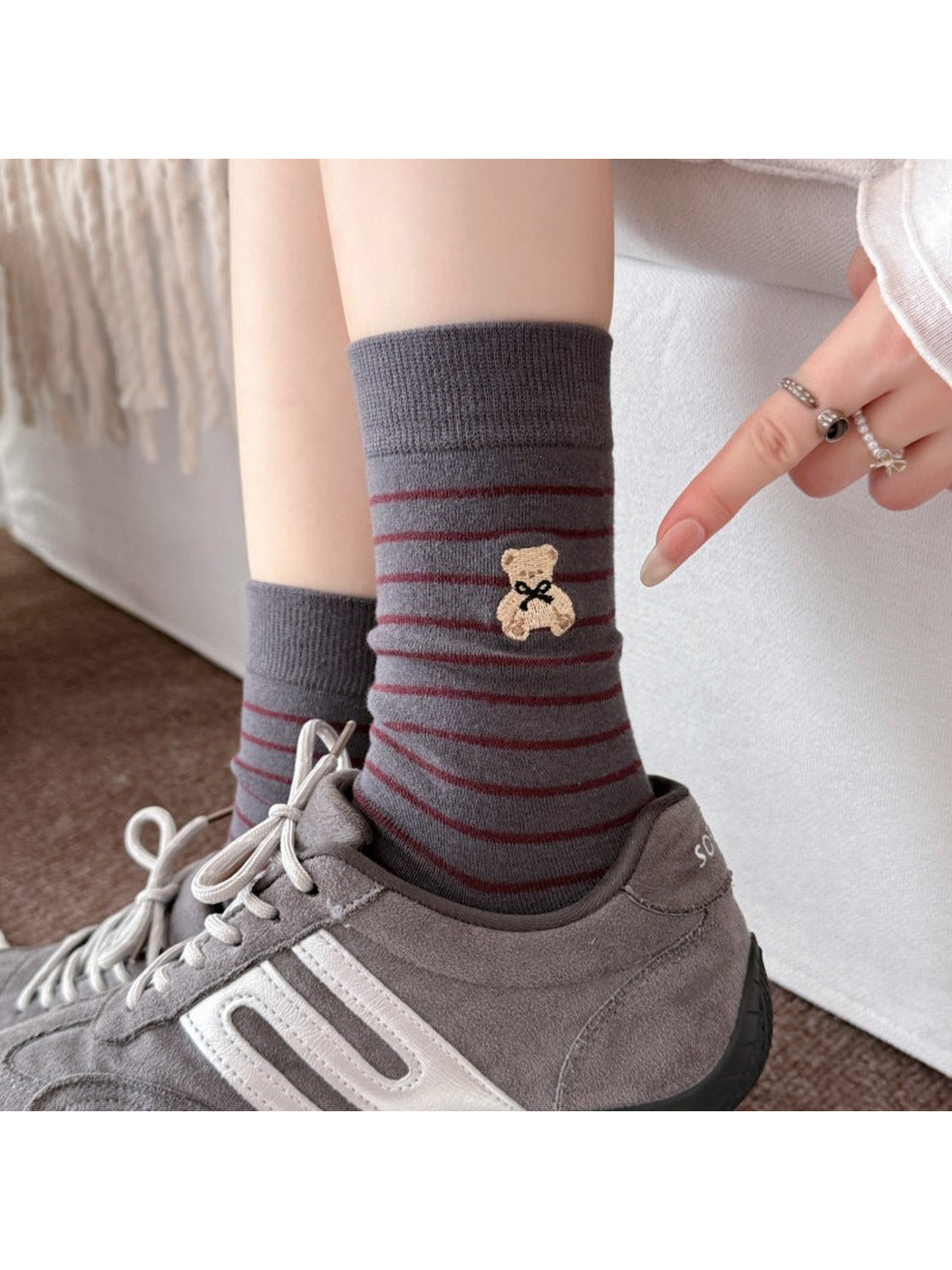 Gray socks with Burgundy stripes worn with gray sneakers, with a finger pointing toward the teddy bear motif.