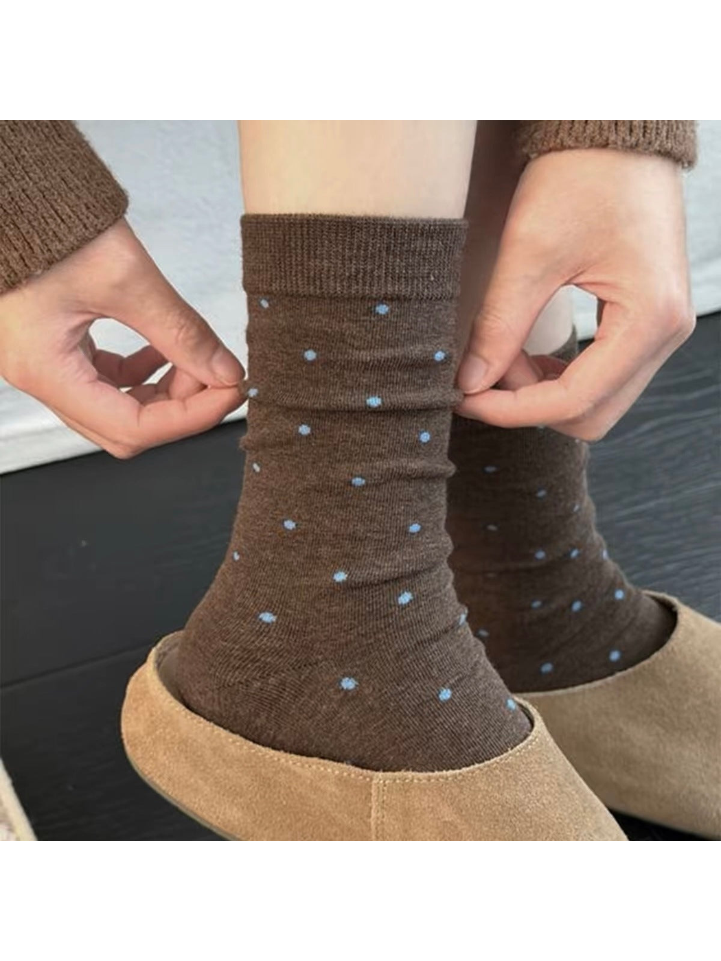 Coffee socks with blue polka dots being adjusted above tan shoes.