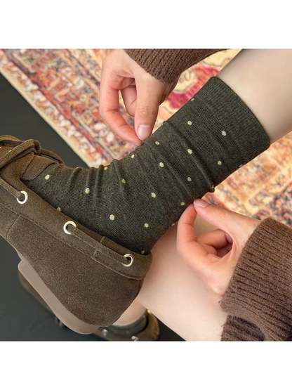 Green polka dot sock being adjusted above a brown lace-up shoe.
