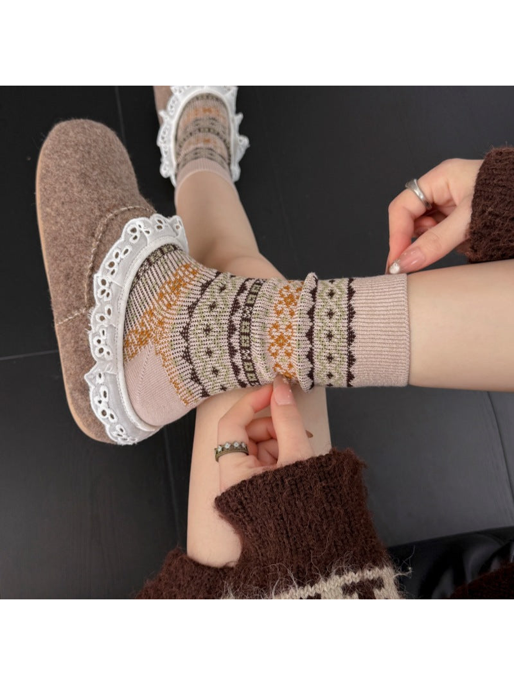 Greige socks with ribbed cuffs and geometric bands worn with slippers, with hands pinching the sock fabric.