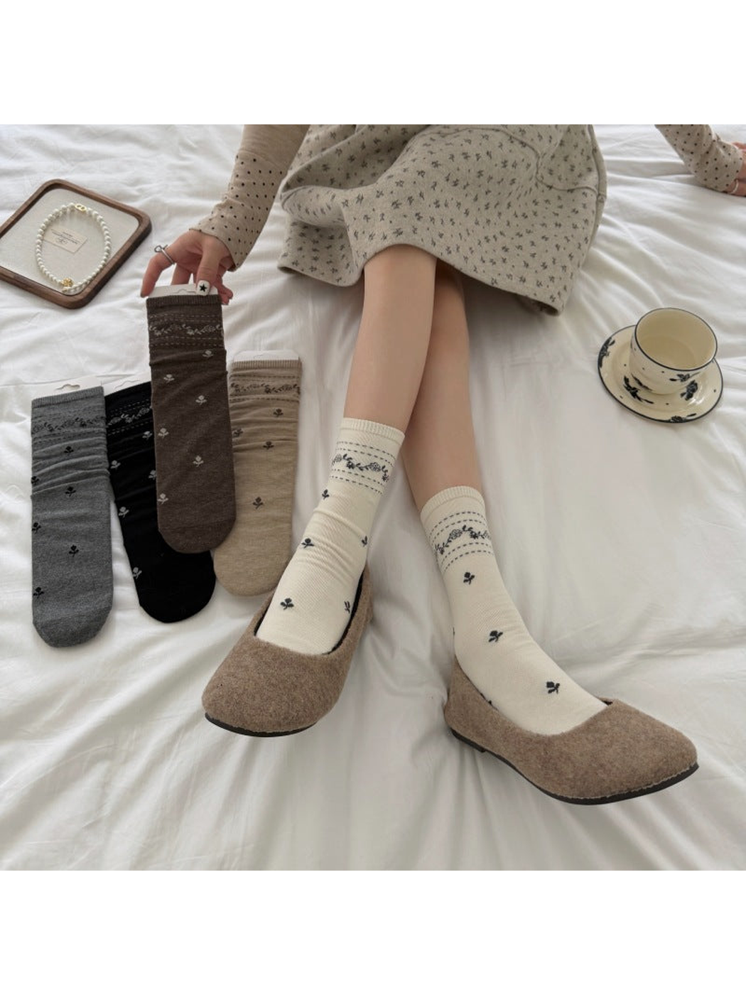 Ivory floral socks worn with shoes while holding a Brown sock beside Gray, Black and Beige socks.