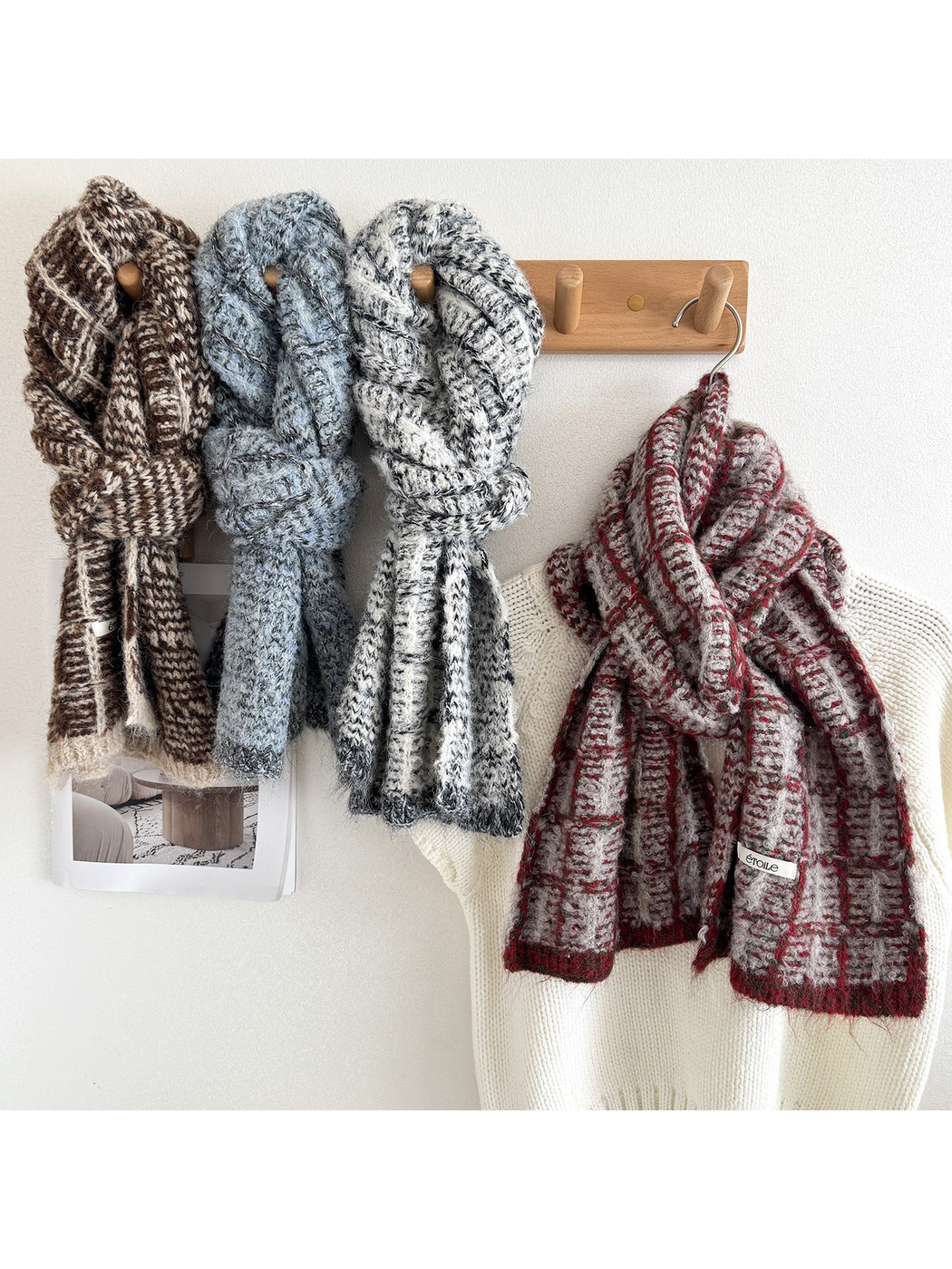 Brown, Blue, and Black / White scarves looped on wooden pegs beside a Burgundy scarf draped over a cream sweater.