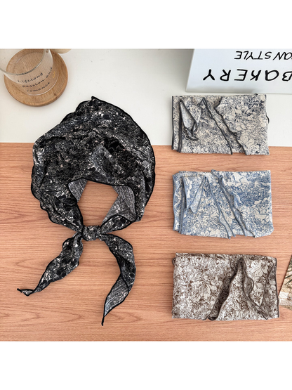 Black floral scarf tied in a loop beside folded Ivory, Blue and Brown scarves.