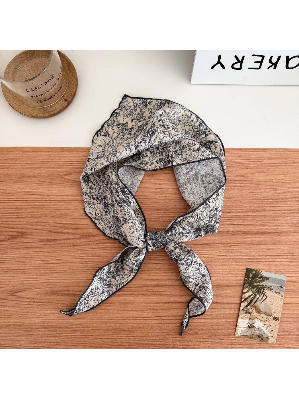 Ivory scarf with dark floral linework and contrasting edges tied in a loop with pointed ends.