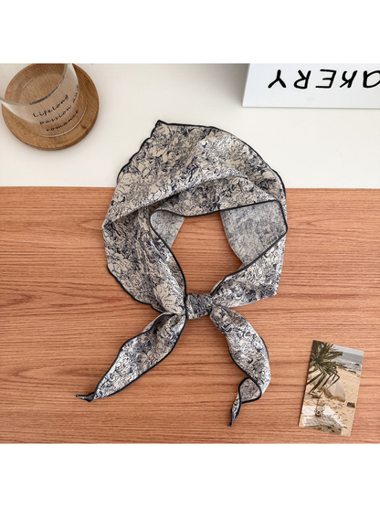 Ivory scarf with dark floral linework and contrasting edges tied in a loop with pointed ends.