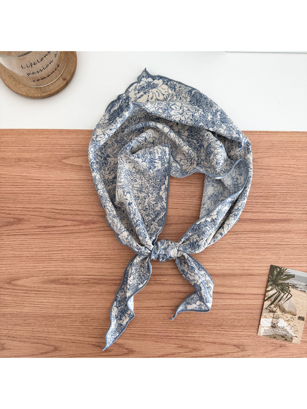 Blue floral scarf on an ivory ground tied in a loop with contrasting edges and pointed ends.