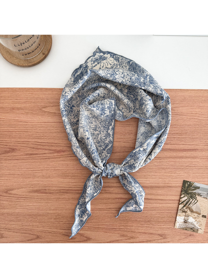 Blue floral scarf on an ivory ground tied in a loop with contrasting edges and pointed ends.